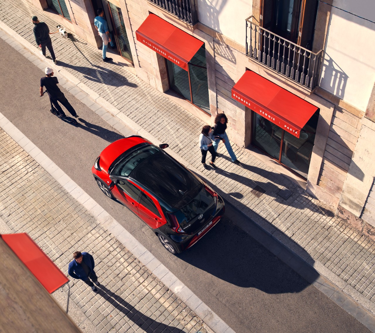 Birds eye view of Chlil Red Aygo X driving down a very narrow city street